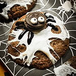 A chocolate cookie decorated with white icing spiderwebs and a sandwich cookie spider with candy eyes.