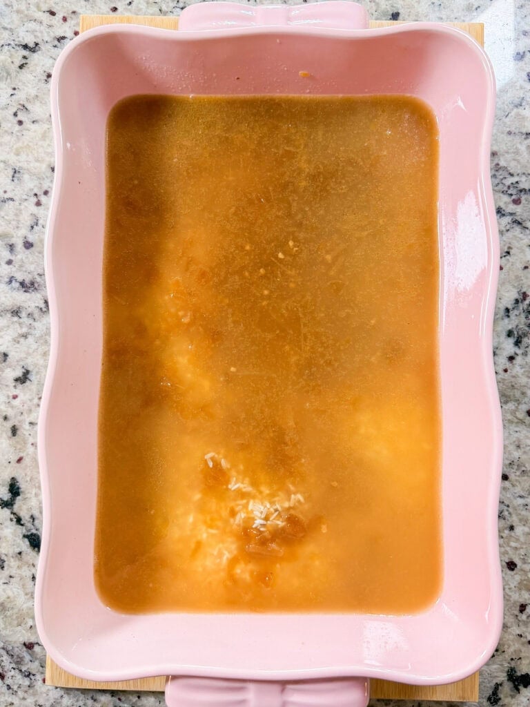 A rectangular pink ceramic baking dish filled with rice and brown liquid.