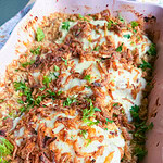 Casserole dish containing chicken topped with melted cheese, crispy fried onions, and fresh parsley, served over a bed of rice.