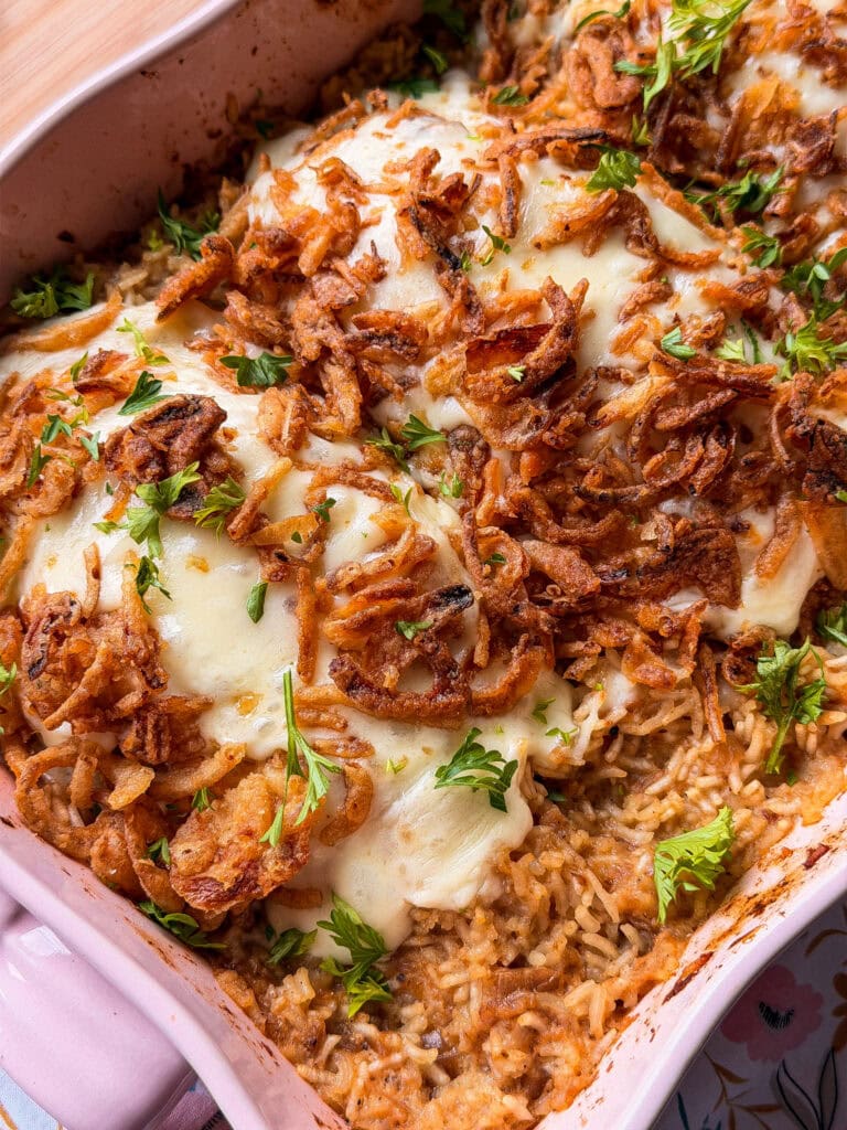 A casserole dish containing rice topped with melted cheese, crispy fried onions, and fresh parsley.