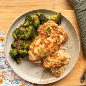 A plate of cheesy chicken and rice casserole topped with crispy onions, served with a side of roasted broccoli.