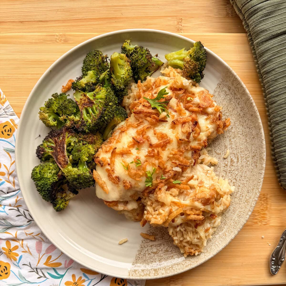 A plate of cheesy chicken and rice casserole topped with crispy onions, served with a side of roasted broccoli.