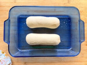Two uncooked dough loaves in a blue glass baking dish.