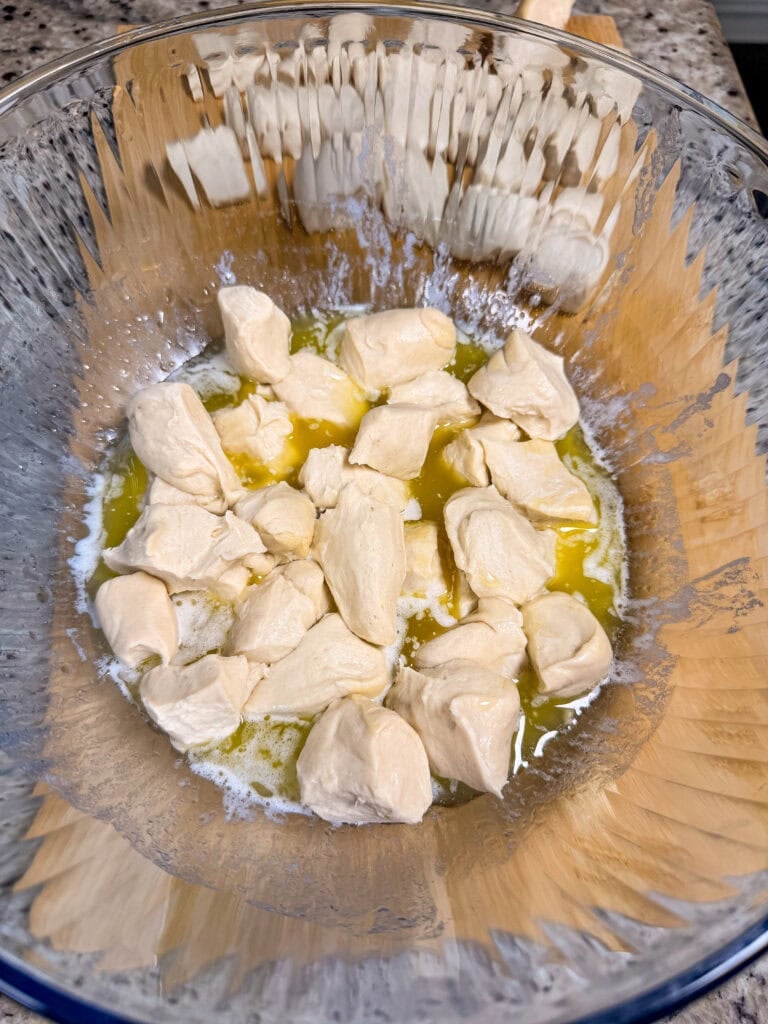 Pieces of raw dough tossed in melted butter in a glass mixing bowl.