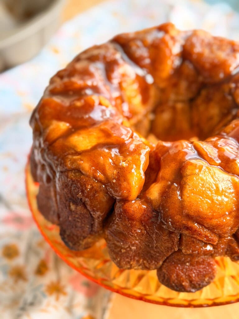 A ring-shaped monkey bread covered in sticky caramel glaze on a glass pedestal.