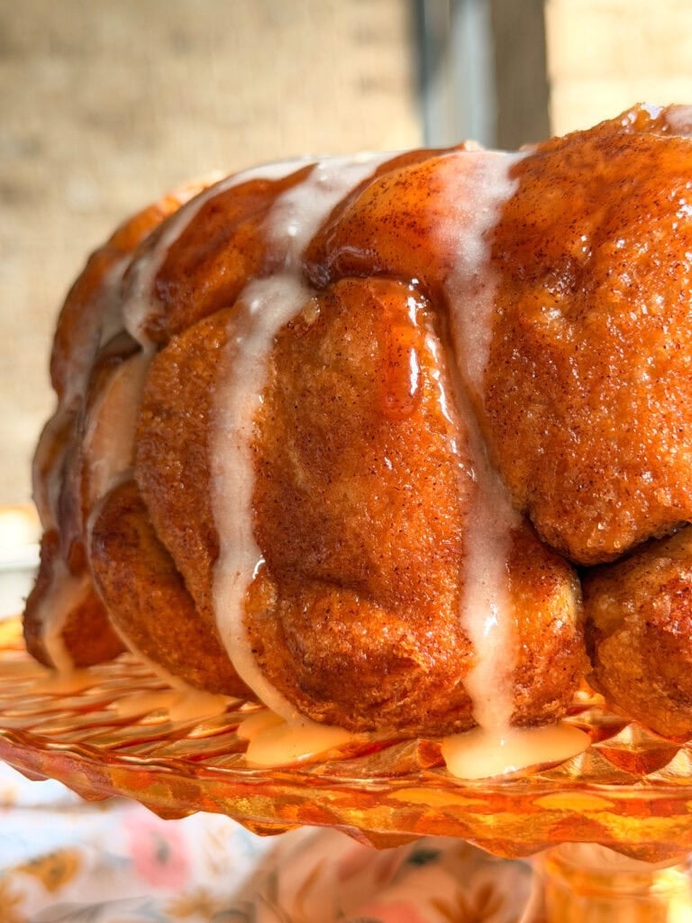 Close-up of a pull-apart monkey bread loaf drizzled with white icing on a decorative amber glass pedestal.