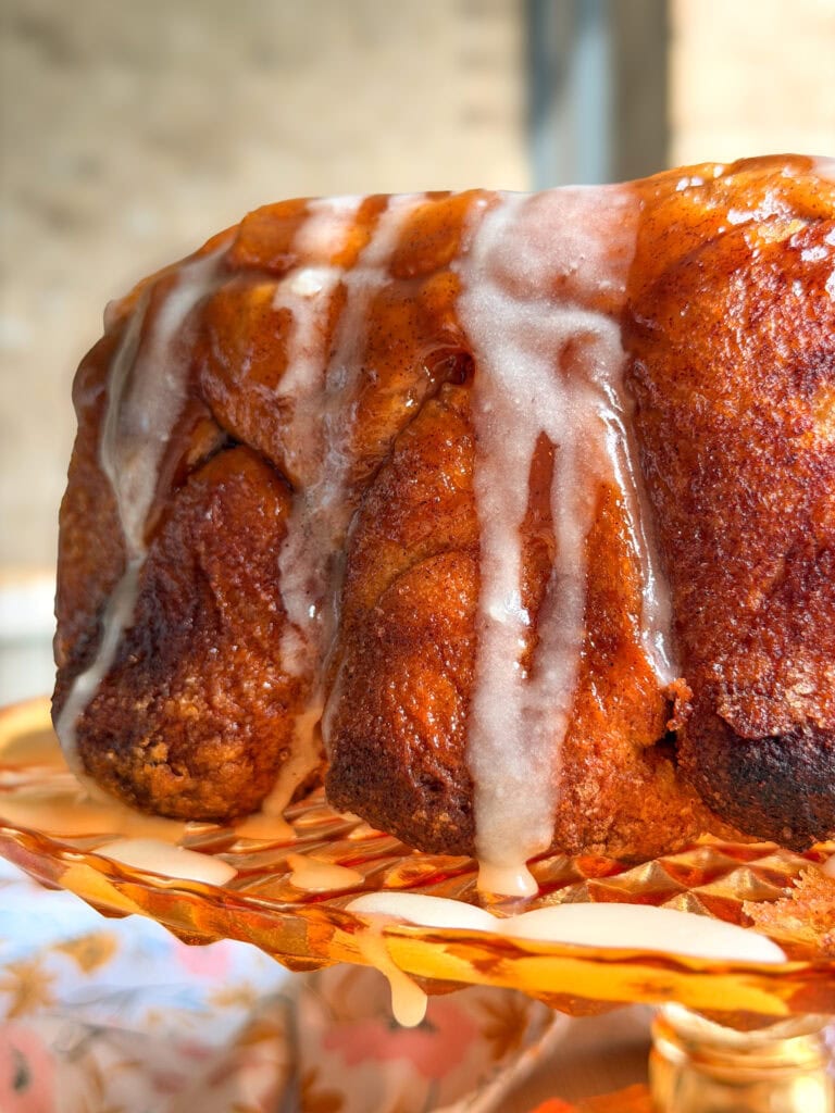 A cinnamon pull-apart bread loaf drizzled with white icing on an orange glass pedestal plate.