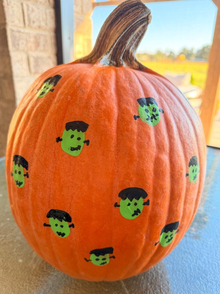 Orange pumpkin decorated with hand-drawn green Frankenstein monster faces.