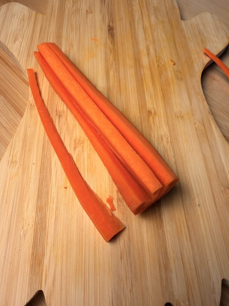 Several carrot sticks on a wooden cutting board.