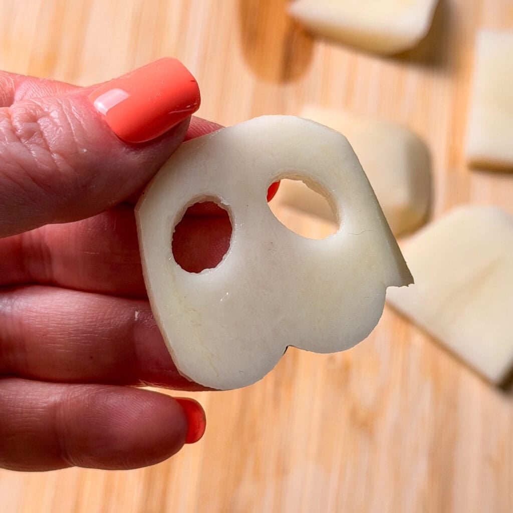 A hand holds a sliced potato piece with two holes that resembles a ghost.