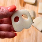A hand holds a sliced potato piece with two holes that resembles a ghost.