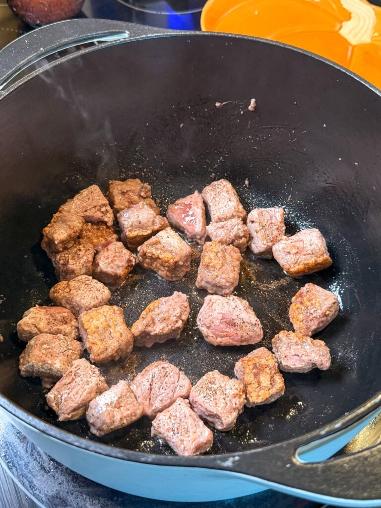 Seasoned cubes of raw beef browning in a black cast-iron pot.