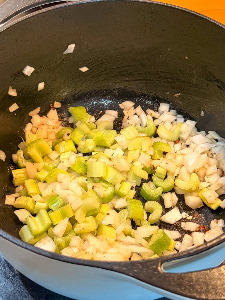 Chopped onions and celery sautéing in a black pot.