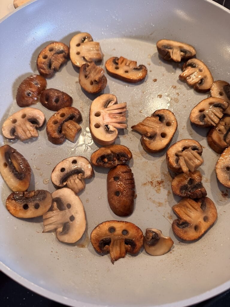Sliced mushrooms sautéing in a light-colored pan.