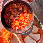 A cast iron pot filled with a hearty stew containing mushrooms and vegetables shaped like ghosts and pumpkins, served with slices of bread.
