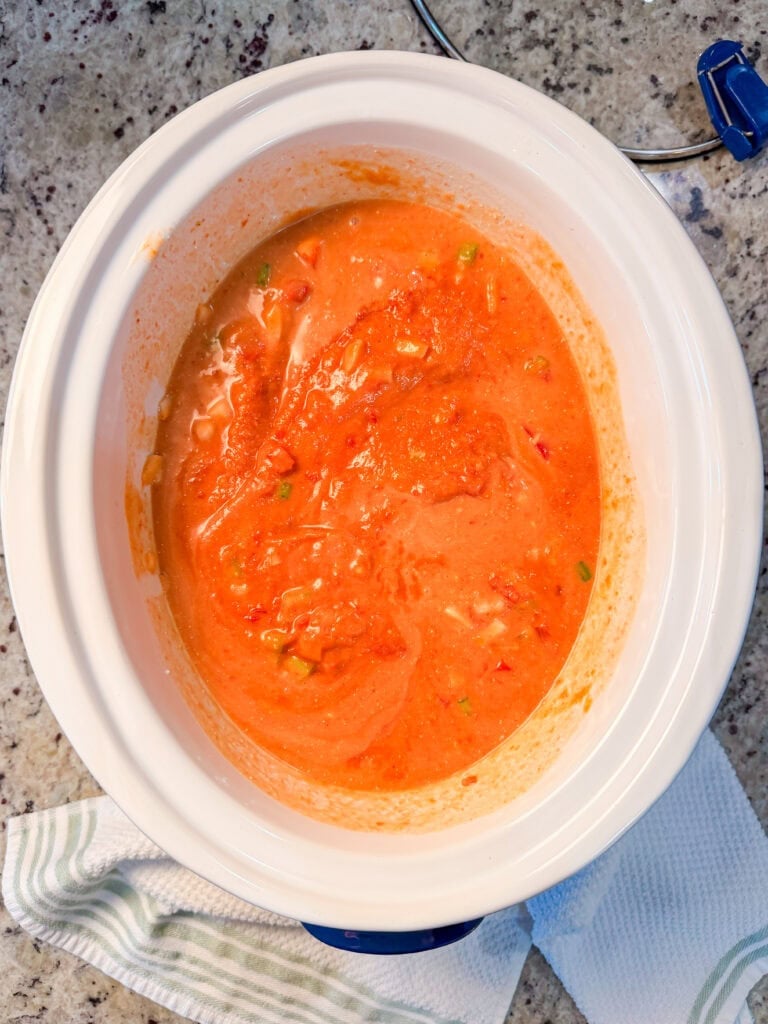 Orange soup with visible vegetable pieces cooking in a white slow cooker.