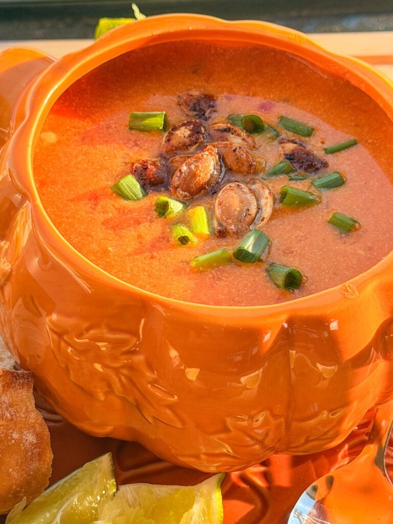 Creamy orange soup topped with roasted seeds and chopped green onions, served in a pumpkin-shaped bowl.
